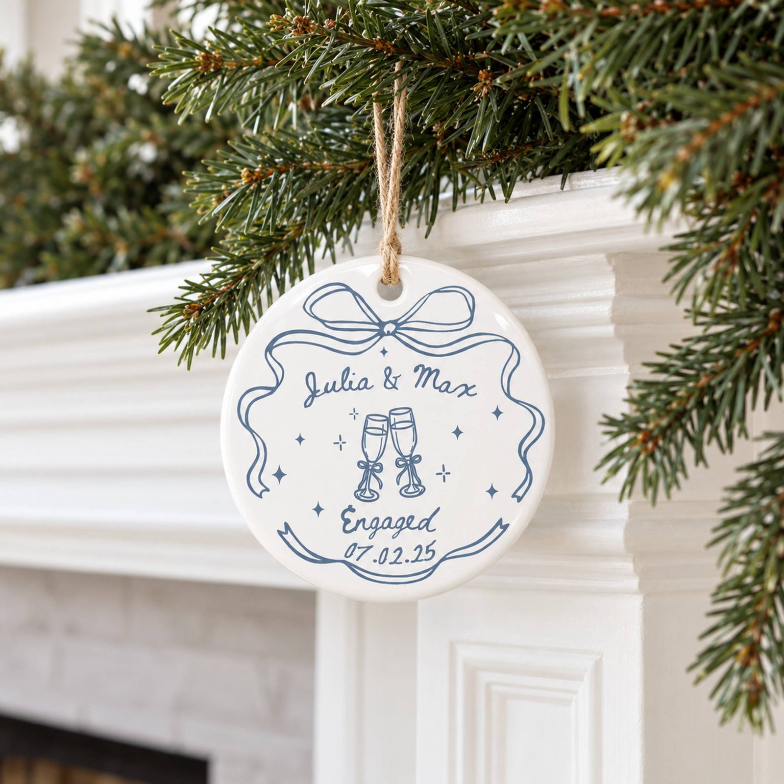 Couple engagement ceramic ornament hanging from pine garland on white holiday mantel