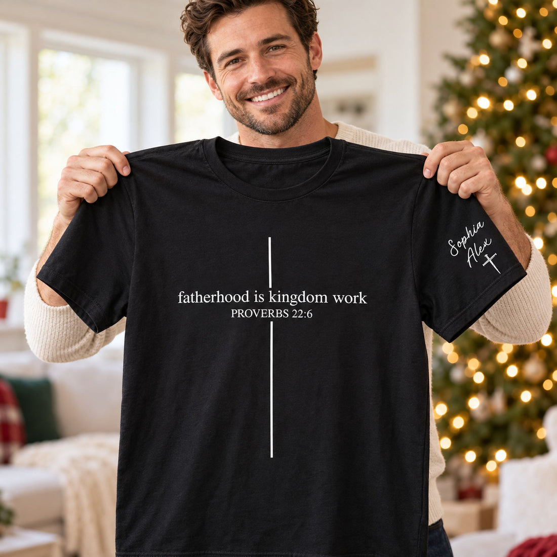 Dad holding personalized Fatherhood Is Kingdom Work black t-shirt with sleeve names on Christmas morning