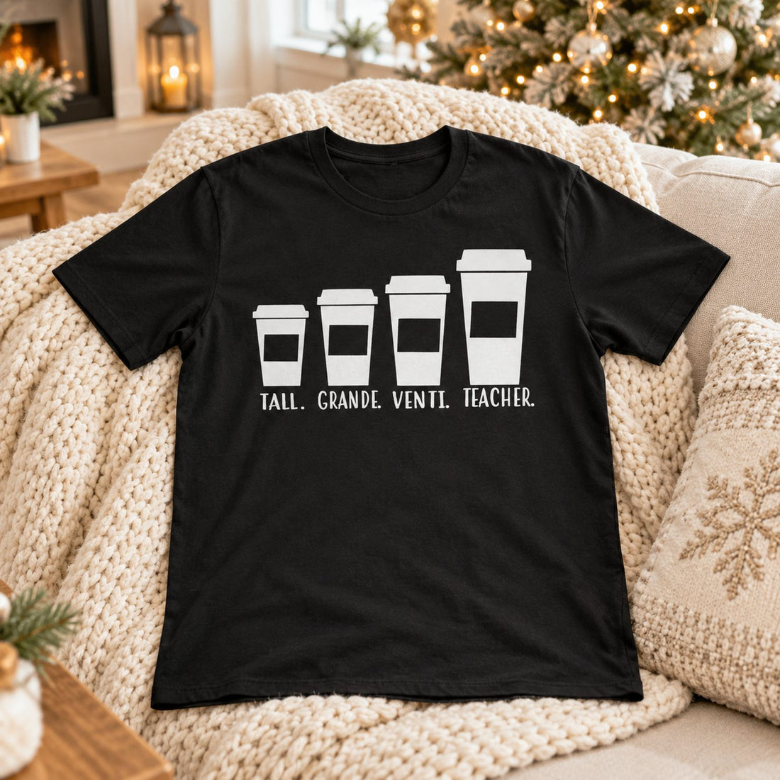 Black funny teacher coffee t-shirt laid on a cozy sofa near a Christmas tree