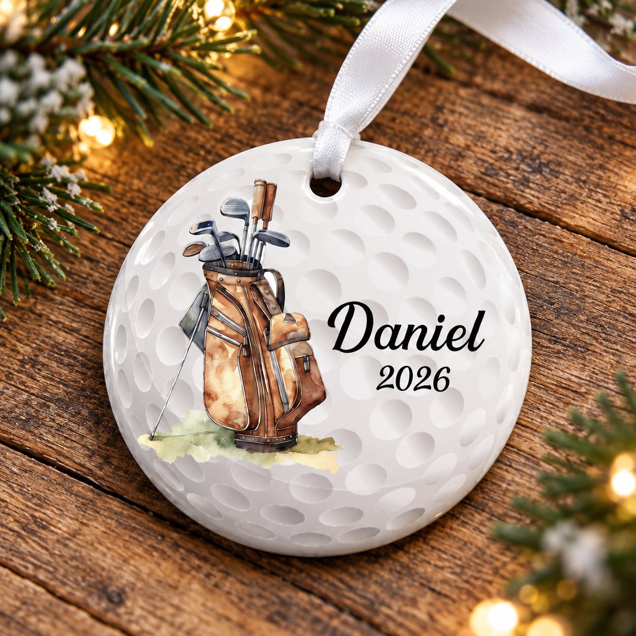 Personalized golf ceramic ornament lying flat on rustic wood with soft Christmas greenery