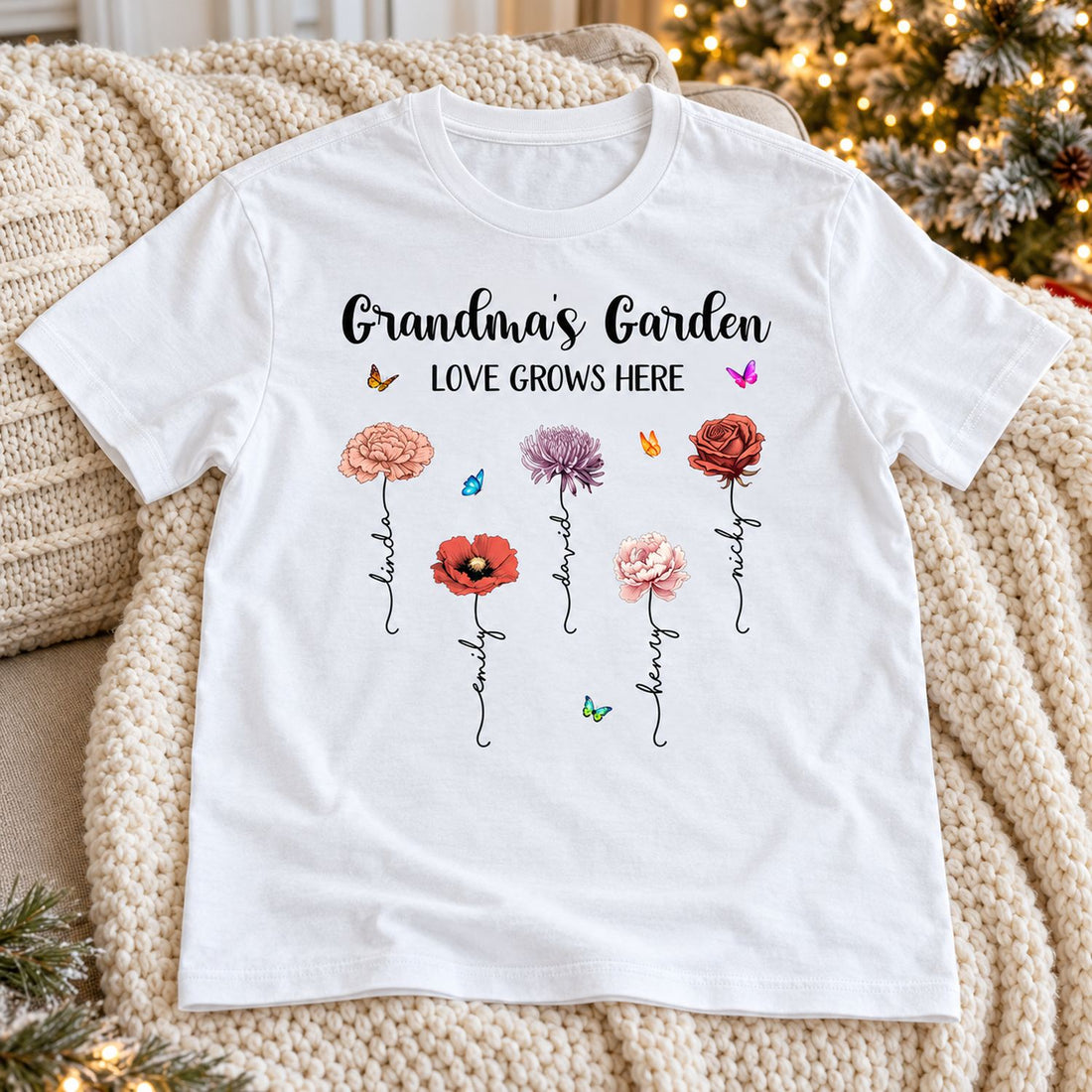 Personalized Grandmas Garden birth flower shirt laid on a cozy sofa with soft Christmas tree lights behind