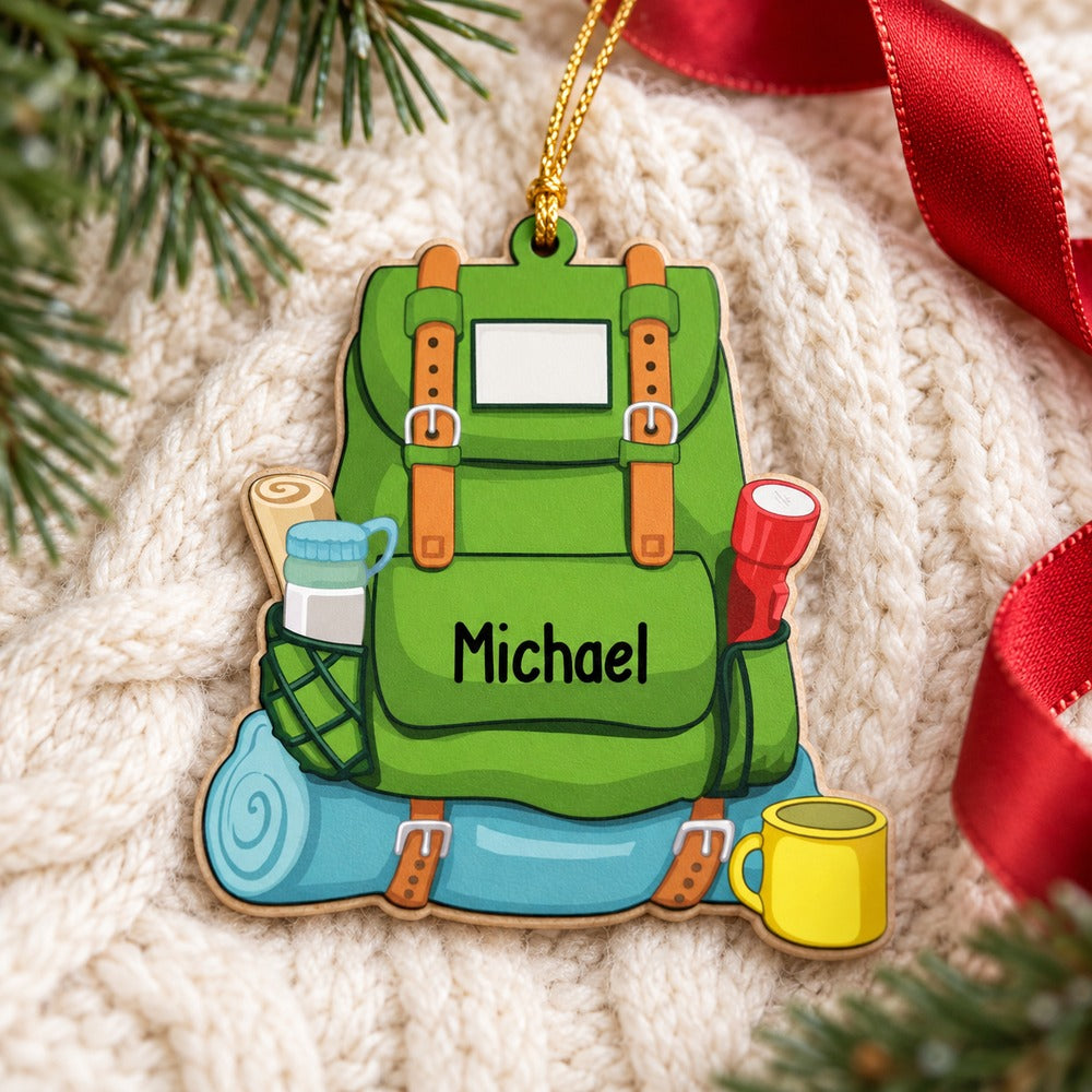 Hiking backpack personalized wood ornament lying flat on a cream knit blanket with pine sprigs