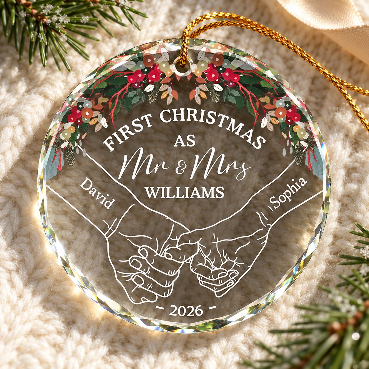 Personalized couple holding hands glass ornament lying flat on a cozy cream knit throw with pine greenery