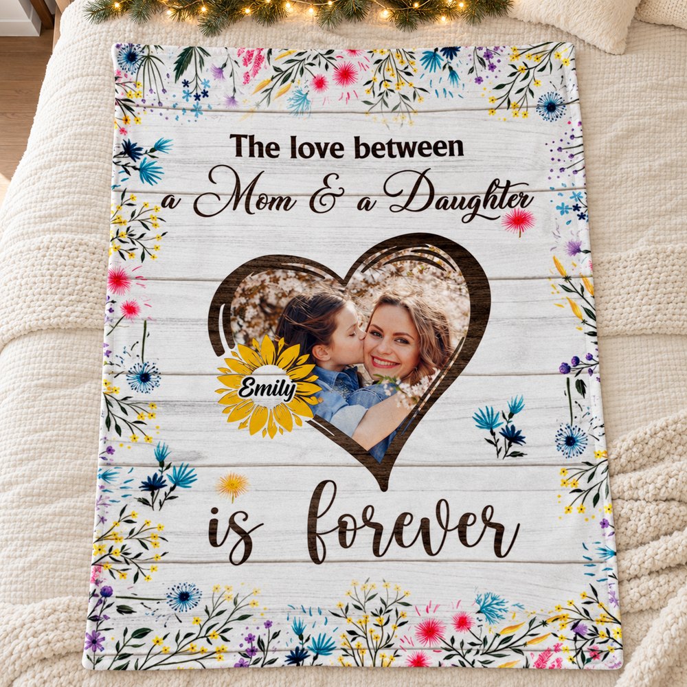 Personalized mom and daughter fleece blanket laid flat on a bed with holiday greenery
