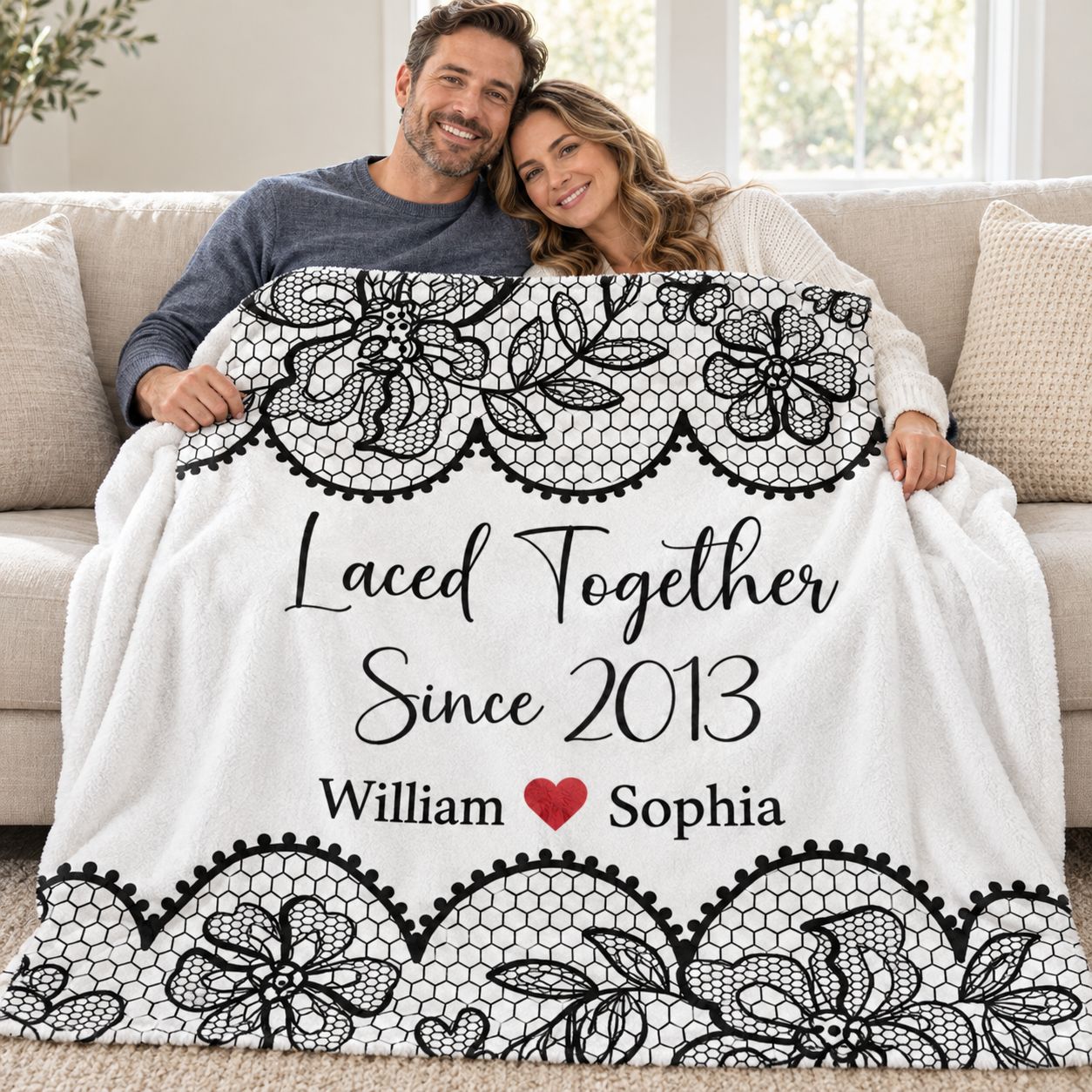 Couple sitting on sofa covered with personalized Laced Together anniversary blanket