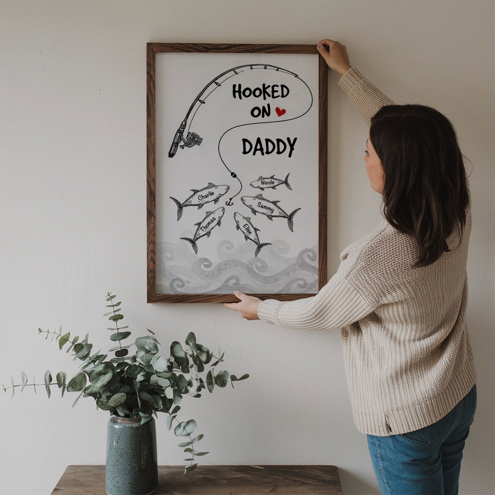 Personalized Fishes Hooked On Daddy Grandpa poster, a woman hanging the framed print on a wall
