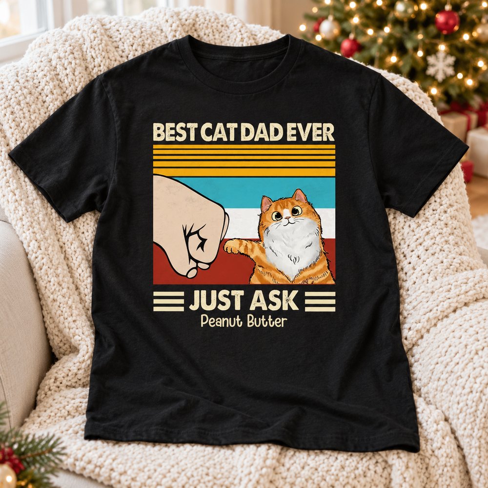 Best Cat Dad Ever personalized t-shirt laid on a cozy armchair near a Christmas tree