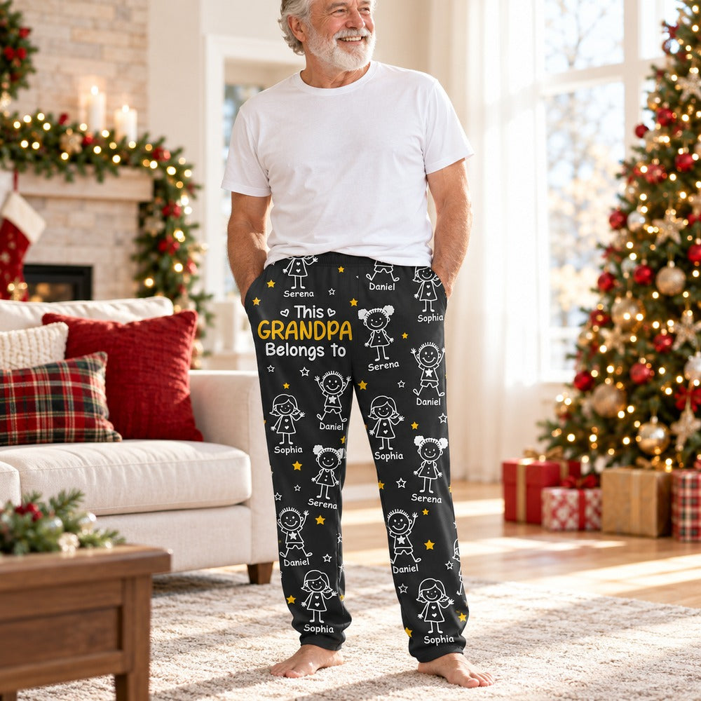 Grandpa standing near a Christmas tree wearing personalized black This Grandpa Belongs To pajama pants