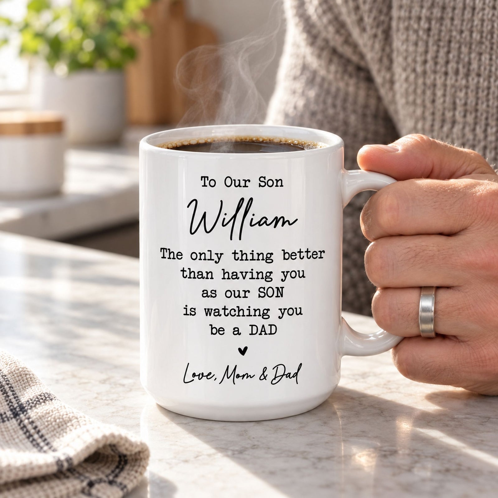 Adult son holding steaming personalized To Our Son ceramic coffee mug in bright kitchen