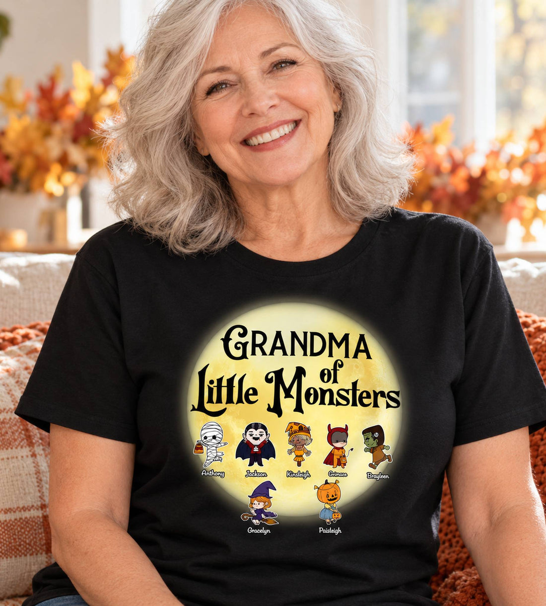Grandma wearing personalized Grandma of Little Monsters black Halloween t-shirt in bright autumn room