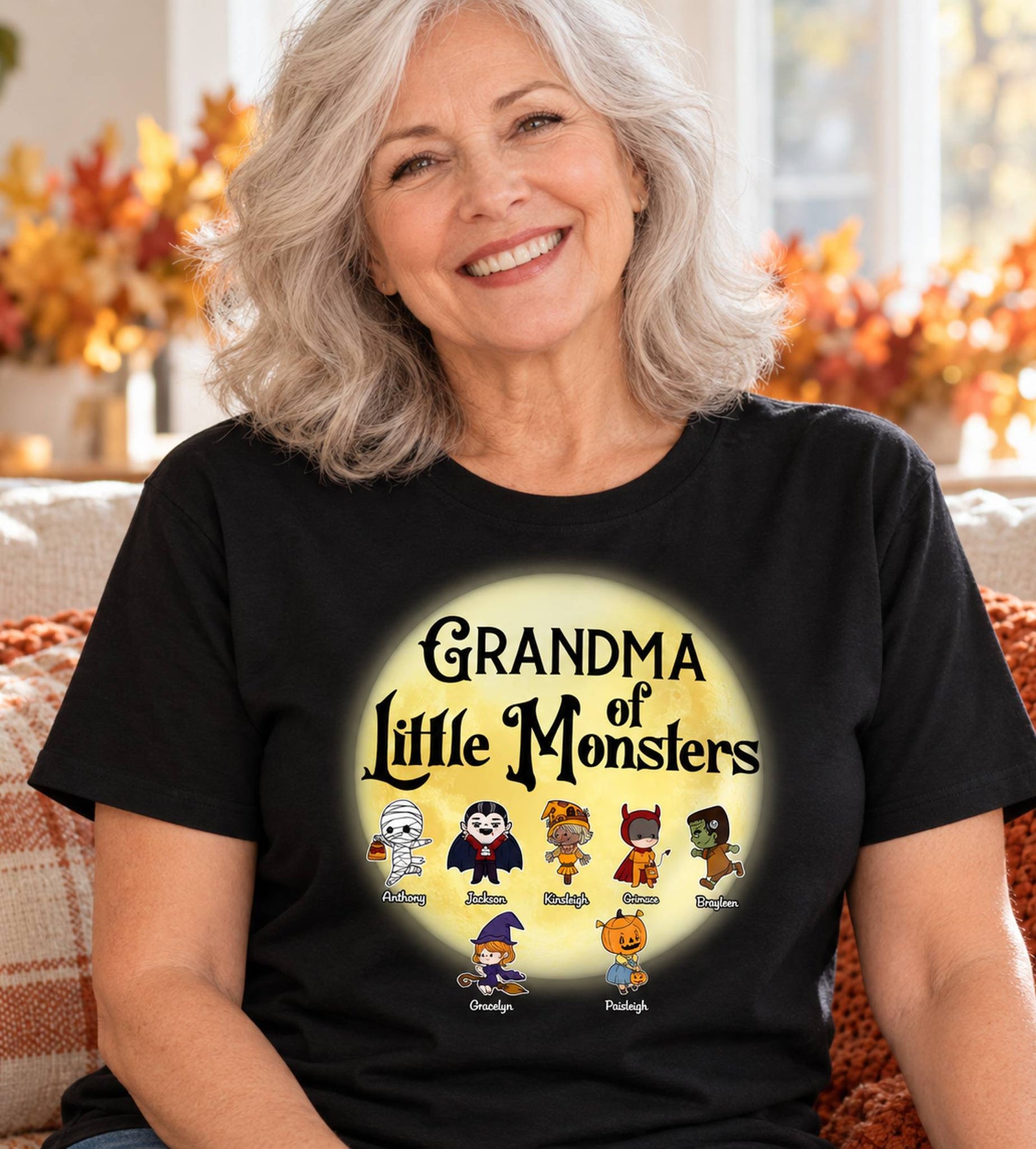 Grandma wearing personalized Grandma of Little Monsters black Halloween t-shirt in bright autumn room