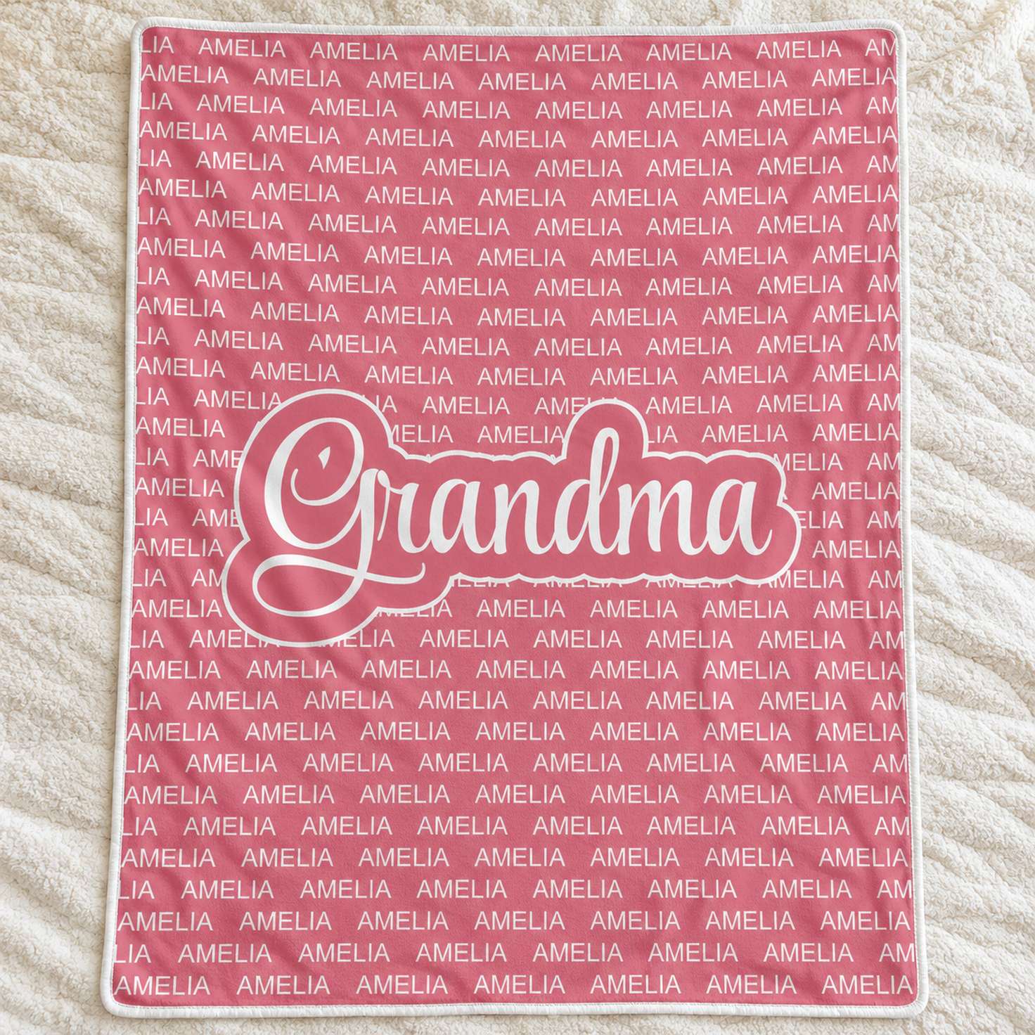 Personalized dusty rose Grandma blanket with repeated Amelia name spread flat on a cream bedspread