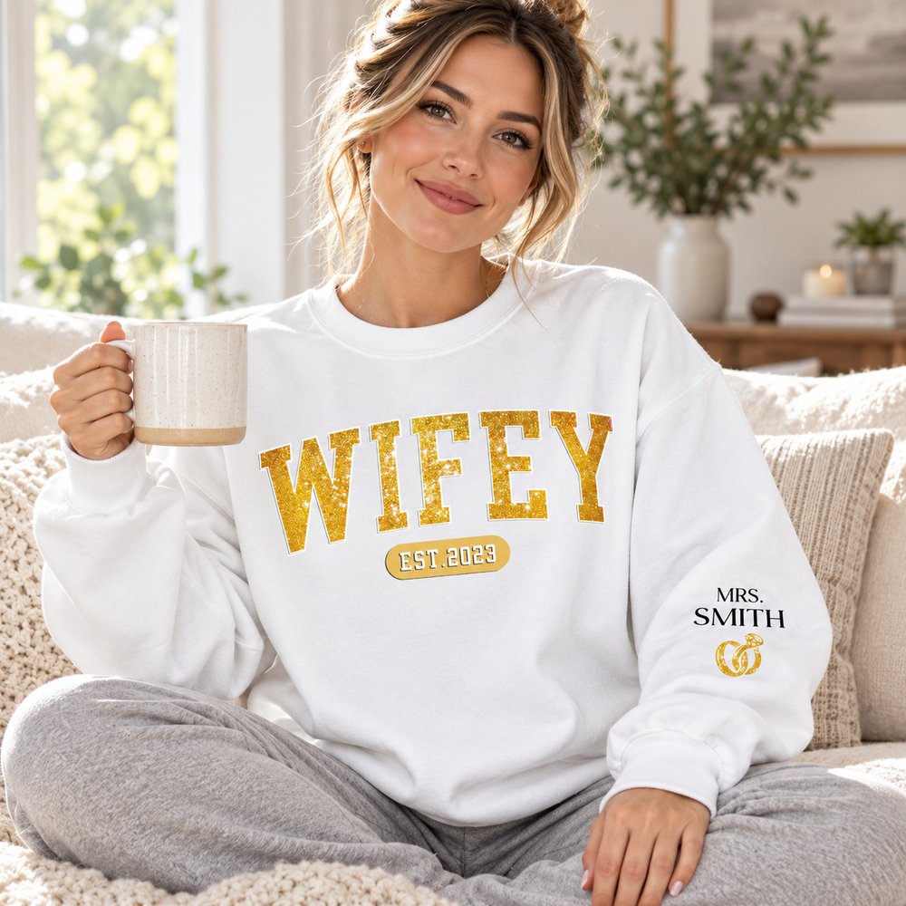 Woman wearing personalized Wifey Est sleeve printed sweater on a bright sofa
